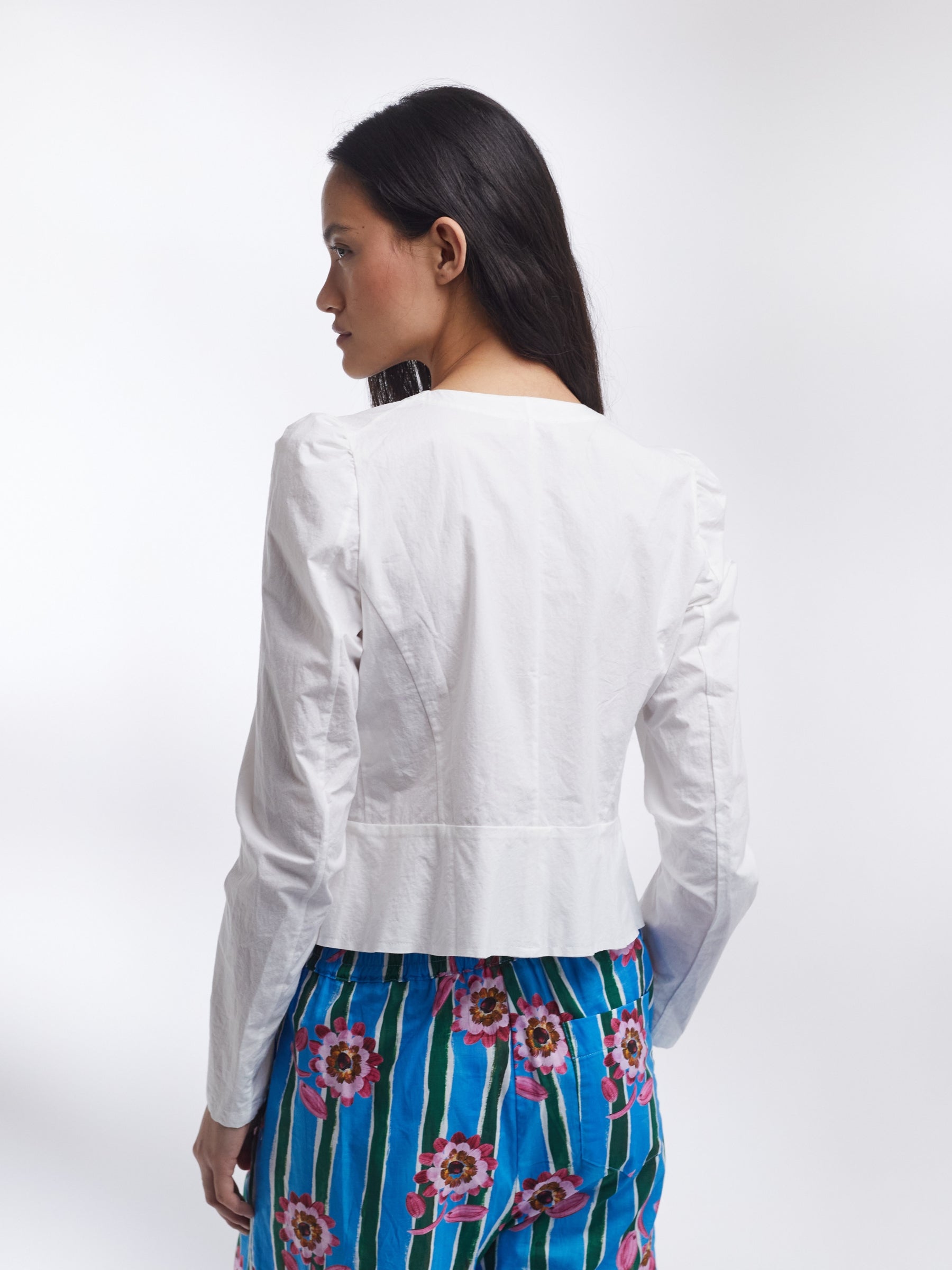 Woman wearing a white jacket and blue floral pants on a white background _ Made in England | Justine Tabak