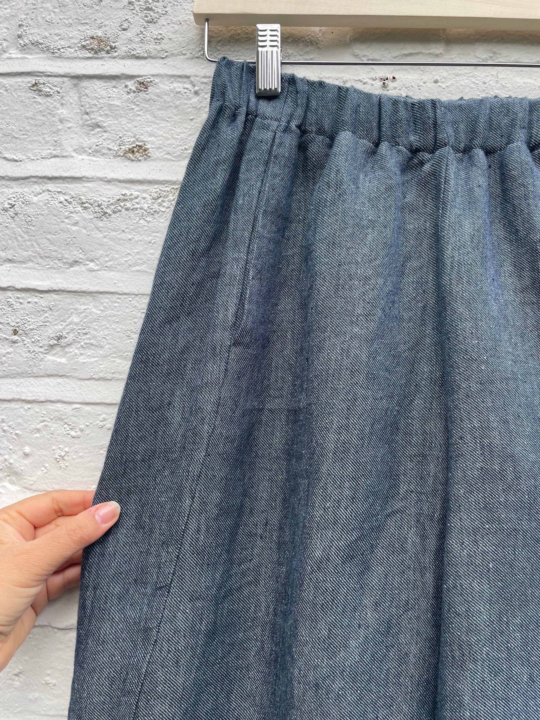 Blue denim skirt held up against a light gray brick wall.